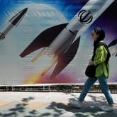 A woman walks past a banner showing missiles being launched, in northern Tehran, Iran, Friday, April 19, 2024. Iran fired air defenses at a major air base and a nuclear site near the central city of Isfahan after spotting drones early Friday morning, raising fears of a possible Israeli strike in retaliation for Tehran's unprecedented drone-and-missile assault on the country. On the missiles, a decorative sign reads: "Allah" (AP Photo/Vahid Salemi)