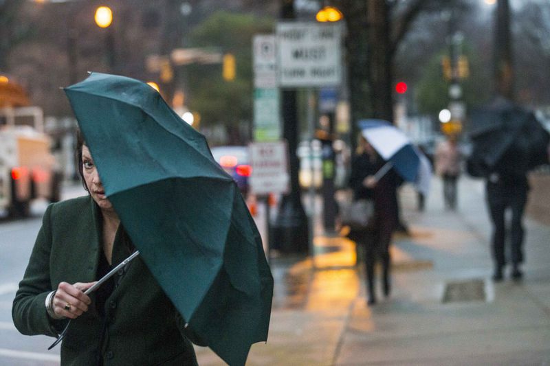 A woman peeks from under her umbrella as she walks along Ponce de Leon Avenue on Tuesday morning.  ALYSSA POINTER / ALYSSA.POINTER@AJC.COM