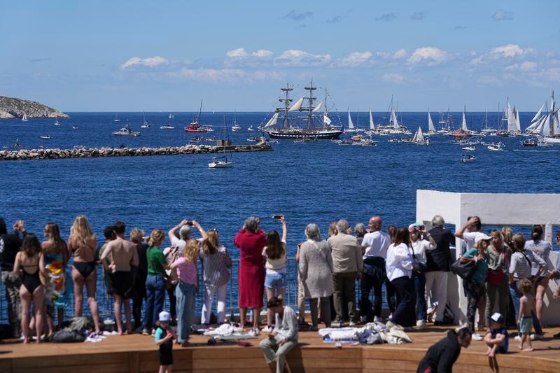 People standing by a swimming pool watch the Belem, the three-masted sailing ship bringing the Olympic flame from Greece, being escorted by other boats when approaching Marseille, southern France, Wednesday, May 8, 2024. After leaving Marseille, a vast relay route is undertaken before the torch odyssey ends on July 27 in Paris. The Paris 2024 Olympic Games will run from July 26 to Aug.11, 2024. (AP Photo/Laurent Cipriani)
