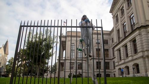 A Georgia Building Authority employee works on a piece of tall fencing Wednesday outside the Georgia Capitol in Atlanta. An 8-foot fence will soon encircle the Capitol as part of a $5 million package of security improvements that will also beef up the Governor's Mansion and the Department of Public Safety's headquarters, according to Gov. Brian Kemp's office. (Alyssa Pointer / Alyssa.Pointer@ajc.com)