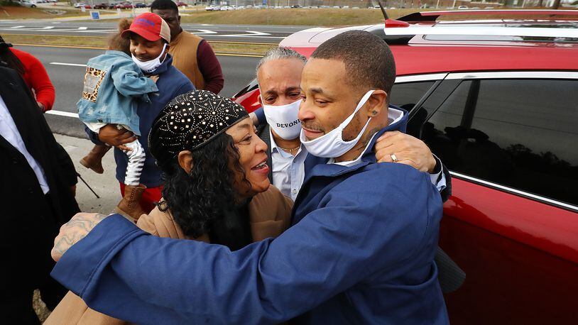 Devonia Inman is embraced by his mother, Dinah Ray, and stepfather, David Ray, after being released from custody Dec. 20, 2021, from the Augusta State Medical Prison (background) after serving 23 years for a wrongful conviction. His charges were dismissed in a murder case. Legislation has been proposed to give Inman more than $1.6 million as compensation for the time he was incarcerated. Curtis Compton / Curtis.Compton@ajc.com