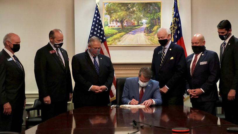 Gov. Brian Kemp signs the elections overhaul into law at the Capitol, flanked by legislative leaders.