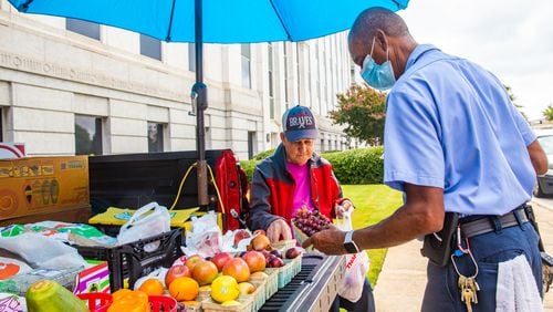 Gerald Reid, seated, who has been a mainstay for more than 50 years around the Atlanta state capitol campus, sells fresh fruits and vegetables out of the back of his truck to Eddie Ferrell, right, who works for the Georgia Building Authority, along Trinity Ave in Downtown Atlanta on Tuesday, Aug. 3, 2021. Reid, 79, comes downtown every week day from Fayetteville after a stop at his local farmers market to sells produce to  those passing by, including Ferrell who is a regular customer and made note that Reid was missed on Monday, when he wasn't able to come.  (Jenni Girtman for The Atlanta Journal Constitution)