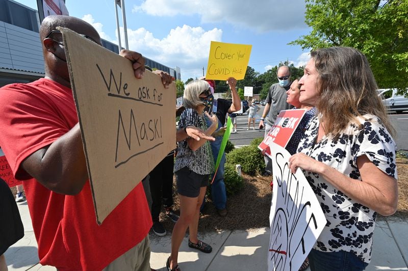 A demonstrator holds a sign that says, "We ask for mask" is confronted by outside the headquarters of the Cobb County School District on Aug. 12, 2021.(Hyosub Shin / Hyosub.Shin@ajc.com)