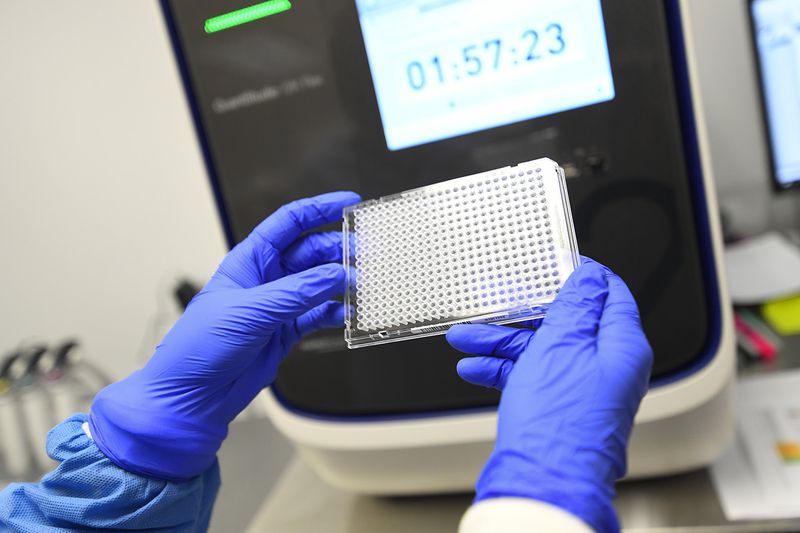 A lab worker holds a plate that will hold samples of possible COVID-19 and will be put in the machine behind it to be analyzed at Ipsum Diagnostics labratory on Monday, March 23, 2020.  (John Amis)