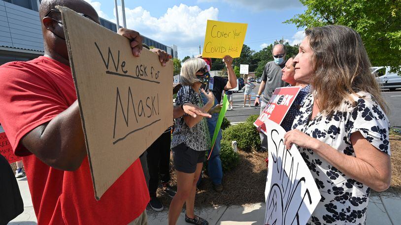 A demonstrator holds a "We ask for mask" sign is confronted outside the headquarters of the Cobb County School District on Aug. 12, 2021.(Hyosub Shin / Hyosub.Shin@ajc.com)