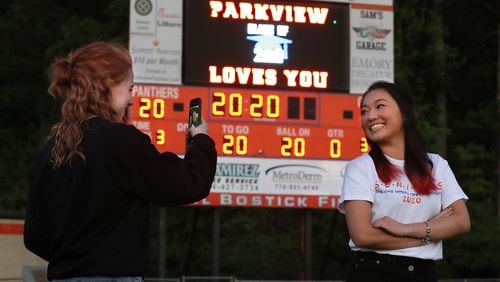 Graduating seniors Jenna Bryant (left) and Kelsey Watkins snap photos of each other in the “Big Orange Jungle,” Hugh Buchanan Field, as it is lit up to honor the class of 2020 at Parkview High School on Tuesday, April 14, 2020, in Lilburn. Every week night at 8:20 pm (20:20 military time) athletic director Nick Gast turns on the scoreboard and stadium lights for 20 minutes and 20 seconds. CURTIS COMPTON / CCOMPTON@AJC.COM
