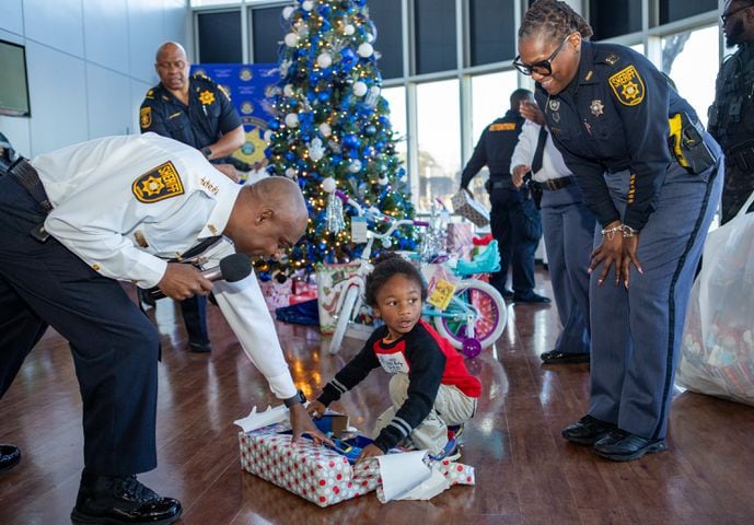 DeKalb County Sheriff’s Office holds the 16th annual Adopt-A-Family celebration on Tuesday, Dec 16, 2023 where Bobby Parks, 6, gets help from Chief Deputy Temetris Akins, left, at the party. Law enforcement officers donate their own money and buy gifts for about a dozen local children.  (Jenni Girtman for The Atlanta Journal-Constitution)