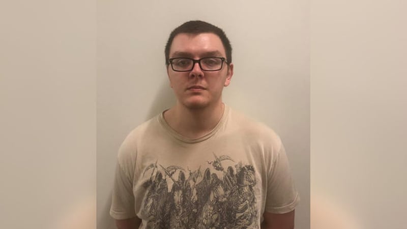 A booking photo of suspected mass bank killer Zepehn Xaver. He appears to be wearing a tan T-shirt depicting the Four Horsemen of the Apocalypse.