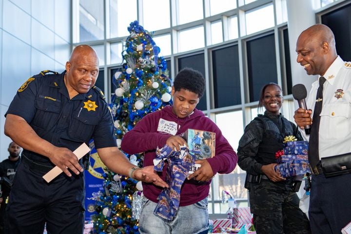 DeKalb County Sheriff’s Office holds the 16th annual Adopt-A-Family celebration on Tuesday, Dec 16, 2023 where Major Ethridge, left, helps 11-year-old James Sims with one of several gifts. Law enforcement officers donate their own money and buy gifts for about a dozen local children.  (Jenni Girtman for The Atlanta Journal-Constitution)