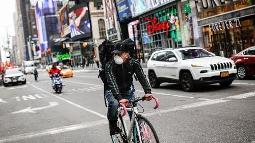 A bicycle delivery worker wears a protective face mask as he rides through a sparsely populated Times Square due to COVID-19 concerns, Friday, March 20, 2020, in New York. (AP Photo/John Minchillo)