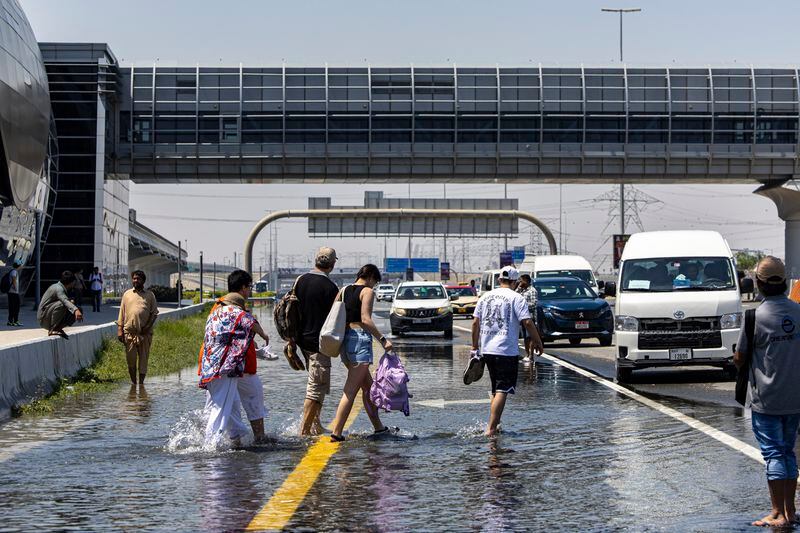 People walk through floodwater caused by heavy rain while waiting for transportation on Sheikh Zayed Road highway in Dubai, United Arab Emirates, Thursday, April 18, 2024. The United Arab Emirates attempted to dry out Thursday from the heaviest rain the desert nation has ever recorded, a deluge that flooded out Dubai International Airport and disrupted flights through the world's busiest airfield for international travel. (AP Photo/Christopher Pike)