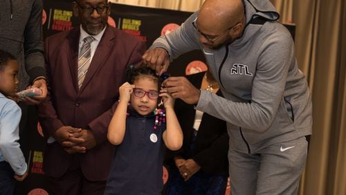 Atlanta Hawks player Vince Carter helps a young girl try on a new pair of glasses.