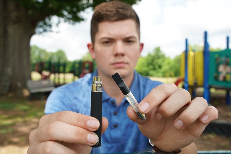 Jay Jenkins holds a Yolo! brand CBD oil vape cartridge alongside a vape pen at a park in Ninety Six, S.C., on Wednesday, May 8, 2019. Jenkins says two hits from the vape put him in a coma and nearly killed him in 2018. Lab testing commissioned by AP showed the vape contained a synthetic marijuana compound blamed for at least 11 deaths in Europe. Jenkins was interviewed as part of an AP investigation into the dark side to the booming CBD industry, in which some people are cashing in by substituting cheap and illegal synthetic marijuana for the natural cannabis extract. (AP Photo/Allen G. Breed)