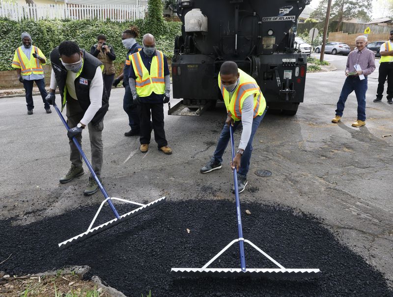 After some instructions, Mayor Andre Dickens (left) and council member Jason Winston try their hand at repairing a pothole.  Dickens and ATLDOT Commissioner Josh Rowan joined the "pothole posse" ahead of Mayor Dickens' 100th day in office In Atlanta on Monday, April 11, 2022.  Mayor Dickens announced at his April 4 State of the City that he was bringing back the pothole posse, a program started by former mayor Shirley Franklin in the early 2000s.(Bob Andres / robert.andres@ajc.com)