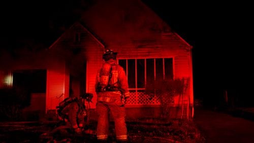 An Atlanta firefighter drags a hose line to a burning home late Friday evening.