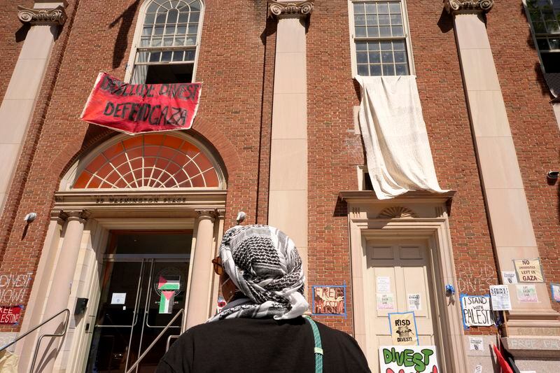 An activist wearing a keffiyeh pauses at an entrance to a building at Rhode Island School of Design, Tuesday, May 7, 2024, in Providence, R.I. Student activists and supporters, who have taken over a portion of the building, are demanding that the school condemn Israel's war effort in Gaza, and that the school divest from investments that benefit Israel. (AP Photo/Steven Senne)