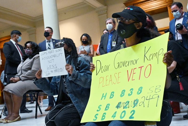 Activists hold signs asking Gov. Brian Kemp, on the day he signed the Georgia's new hate-crimes legislation, to veto House Bill 838, a measure meant to create new protections for police. Kemp signed HB 838 into law Wednesday. (Hyosub Shin / Hyosub.Shin@ajc.com)