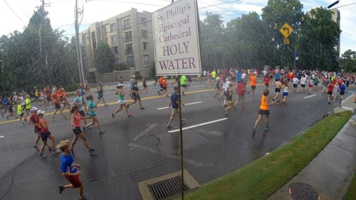 Some runners go for a quick blessing under the holy water sprinkler at the Cathedral of St. Philip as they make their way down Peachtree Road in Buckhead during the AJC Peachtree Road Race on July 4, 2014. AJC FILE PHOTO