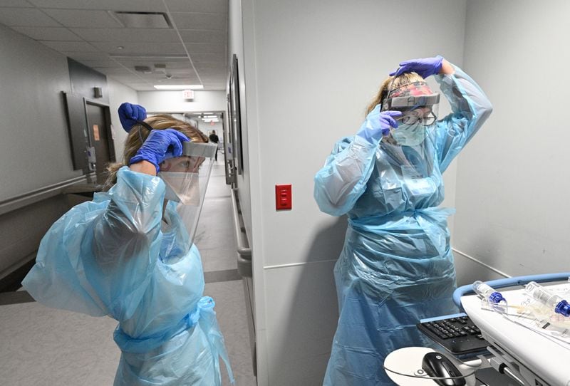 Registered Nurse Alexandra Desloovere, right, and nursing student Kelsey Park put on PPE before they attend to a COVID-19 patient at Memorial Health's Heart and Vascular Institute in Savannah. The delta wave has taken an emotional toll on workers, and staff burnout is a problem high on the minds of hospital administrators. (Hyosub Shin / Hyosub.Shin@ajc.com)