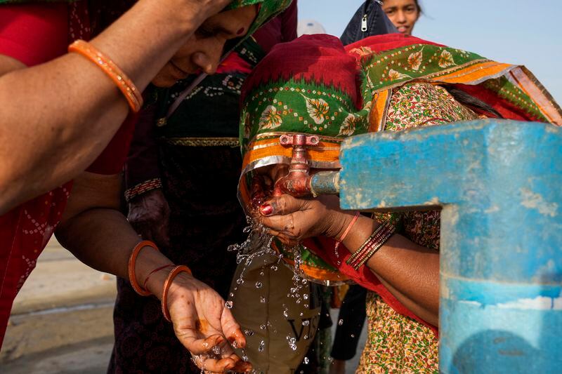 FILE - Women drink water from a public tap near the River Ganges on a hot day at Sangam in Prayagraj, Uttar Pradesh state, India, May 2, 2024. In a world growing increasingly accustomed to wild weather swings, the last few days and weeks have seemingly taken those environmental extremes to a new level. (AP Photo/Rajesh Kumar Singh, File)
