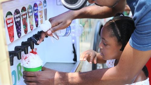 Griffith James helped his five-year-old daughter Kelci add flavoring to her Kona Ice as local artisans and national classics presented their best products at the 4th Annual Atlanta Ice Cream Festival at Piedmont Park in Atlanta on Saturday, July 26, 2014. There was a variety of health /wellness agencies, fitness routines, vendors, entertainment, bands and fun family activities. (Photo by Phil Skinner)