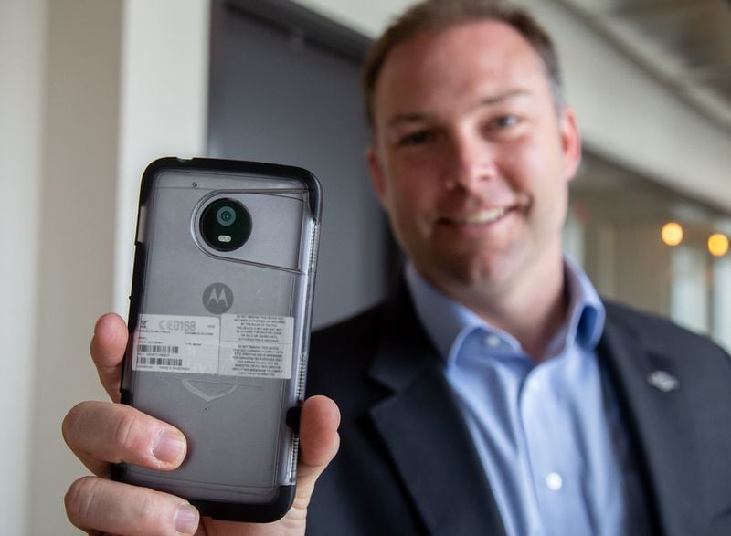Chris Lindenau, chief revenue officer of the Decatur-based company Utility Associates, Inc., holds a Motorola phone they have adapted to work with the company’s body-worn cameras system at there headquarters in Decatur Thursday, April 4, 2019. Atlanta Public Schools police officers began using the devices in March. STEVE SCHAEFER / SPECIAL TO THE AJC