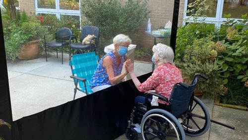 Susan Merritt, left, visits her mother, Rosie Gamel,  in August at A.G. Rhodes’ Wesley Woods location. A divider is used to allow families to visits residents as safely as possible during the coronavirus pandemic. (HANDOUT)