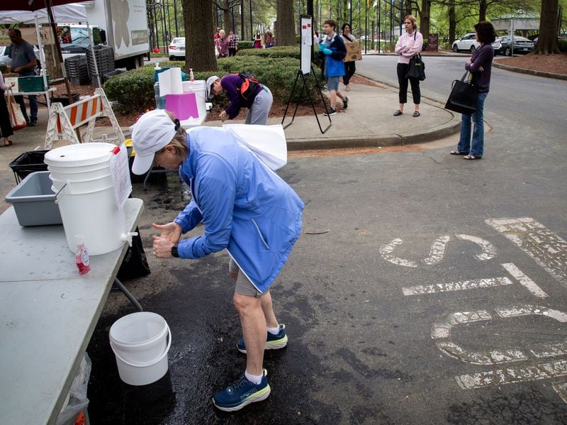 Tammy Bregman washes her hands before entering the Freedom Farmers Market at the Carter Center in Atlanta on March 28, 2020. Buckets of water and hand soap were supplied to everyone coming into the market. STEVE SCHAEFER / SPECIAL TO THE AJC