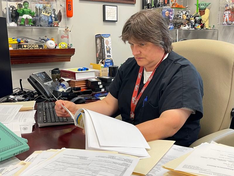 Carol Terry, medical examiner for Gwinnett County, sits in her Lawrenceville office and flips through the pages of deaths caused by fentanyl and other synthetic opioids in 2020 and 2021. (Tyler Wilkins / tyler.wilkins@ajc.com)