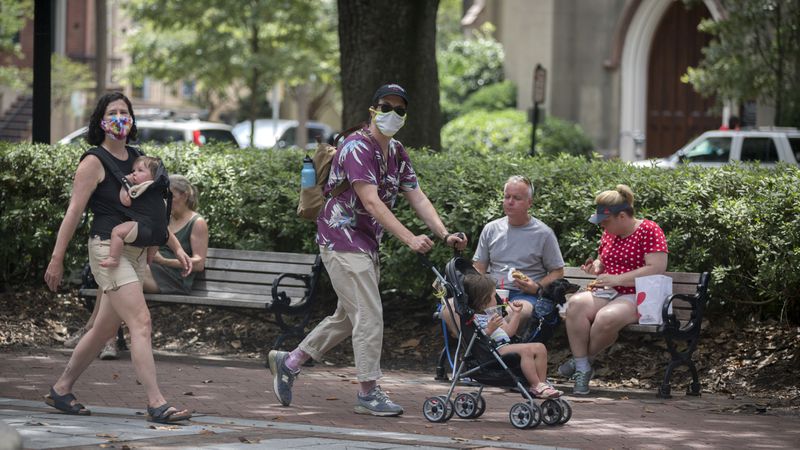 A family wearing masks walk through one of Savannah's historic squares while other visitors eat on a bench nearby. Savannah was the first major city in Georgia to require the use of face masks to contain the coronavirus. (AJC Photo/Stephen B. Morton)
