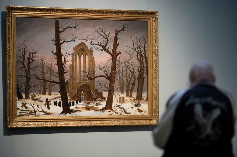 A man sits in front of a copy of Caspa David Friedrich's painting Monastery Cemetery In Snow' during a press preview of the exhibition 'Caspar David Friedrich. Infinite Landscapes' at the Alte Nationalgalerie museum in Berlin, Germany, Wednesday, April 17, 2024. A major show of Caspar David Friedrich's iconic landscapes that marks the 250th anniversary of his birth is opening in Berlin, the city where he made his breakthrough and where an exhibition in 1906 kicked off an an enduring revival in interest in the German Romantic master. (AP Photo/Markus Schreiber)