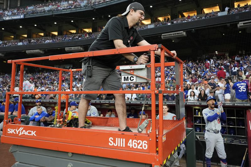 A groundkeeper moves a lift past the Los Angeles Dodgers dugout as Dodgers' Mookie Betts, right, cheers, in preparation to remove swarm of bees gather on the net behind home plate delaying the start of a baseball game against the Arizona Diamondbacks, Tuesday, April 30, 2024, in Phoenix. (AP Photo/Matt York)