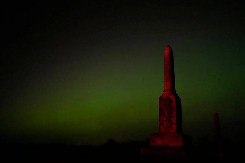 An old tombstone stands against the northern lights at a cemetery early Saturday, May 11, 2024, near Skidmore, Mo. (AP Photo/Charlie Riedel)