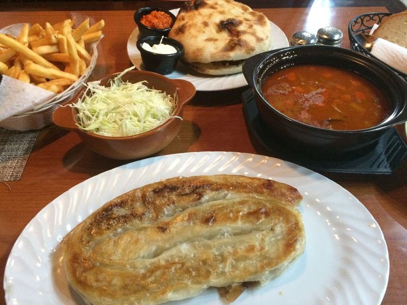 A lunchtime spread at Euro Gourmet Grill includes the meat-filled pastry borek (front), a Bosnian beef “roast” that’s really a stew (right), a pita sandwich filed with sausages (rear), fries, and sour cabbage. CONTRIBUTED BY WENDELL BROCK