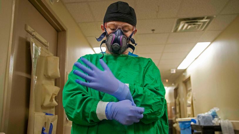 A Tanner Health System nurse puts on protective gloves as she prepares to enter a patient's room on the Covid-19 isolation floor at the Carrollton hospital. Leaders of the hospital told the AJC they could alleviate overcrowding there if insurance companies processed discharge requests faster. (Alyssa Pointer / Alyssa.Pointer@ajc.com)
