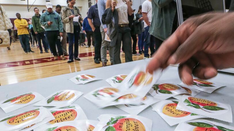 Poll worker DeCarlos Bennett hands out stickers to voters at Grady High School in Atlanta in 2016. JOHN SPINK /JSPINK@AJC.COM