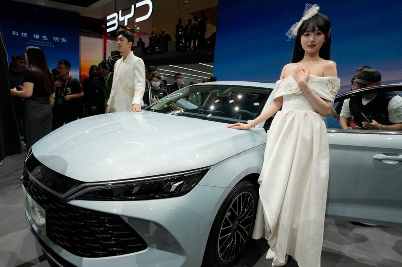 Models pose near the BYD Qin L Dmi unveiled during Auto China 2024 held in Beijing, Thursday, April 25, 2024. China's largest EV maker, BYD has been expanding rapidly into overseas markets, launching its low-priced Dolphin Mini, sold as the Seagull in China, in Latin American markets this year. (AP Photo/Ng Han Guan)