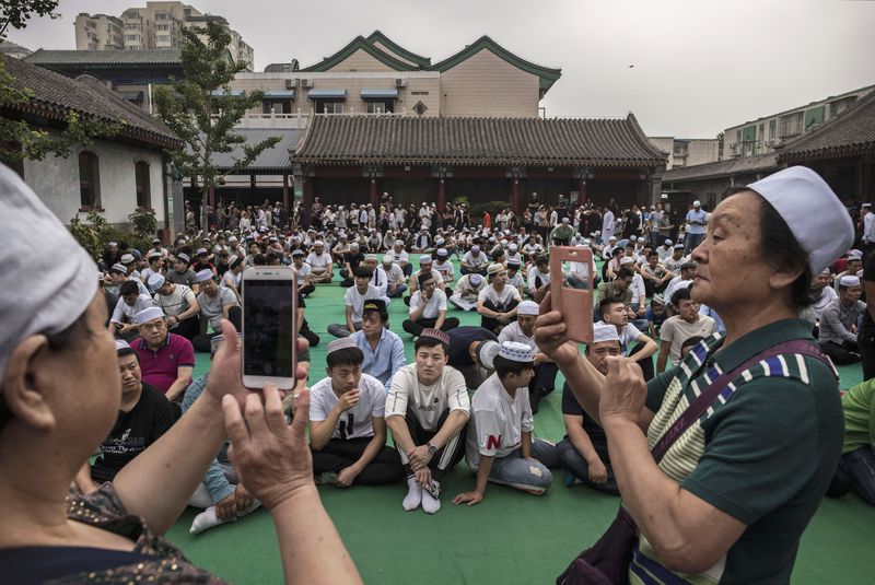 BEIJING, CHINA - JUNE 16: Chinese Hui Muslim men take photos as they wait on a carpet before Eid al-Fitr prayers marking the end of the holy fasting month of Ramadan at the historic Niujie Mosque on June 16, 2018 in Beijing, China. Islam in China dates back to the 10th century as the legacy of Arab traders who ventured from the Middle East along the ancient Silk Road. Of an estimated 23 million Muslims in China, roughly half are Hui, who are ethnically Chinese and speak Mandarin. China's constitution provides for Islam as one of five 'approved' religions in the officially atheist country though the government enforces severe limits. Worship is permitted only at state-sanctioned mosques and proselytizing in public is illegal. The Hui, one of 55 ethnic minorities in China (along with the Han majority), have long nurtured a coexistence with the Communist Party and is among the minority groups with political representation at various levels of government. The Hui Muslim population fast from dawn until dusk during Ramadan and it is believed there are more than 20 million members of the community in the country. (Photo by Kevin Frayer/Getty Images)