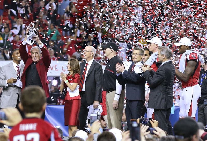 As confetti falls in the Georgia Dome, owner Arthur Blank hoists the trophy that’s awarded the winner of the NFC championship after the Falcons’ recent victory over the Green Bay Packers, sending them to the Super Bowl. With Blank (from left) are team president Rich McKay, coach Dan Quinn, general manager Thomas Dimitroff, quarterback Matt Ryan and wide receiver Julio Jones. (Curtis Compton/ccompton@ajc.com)