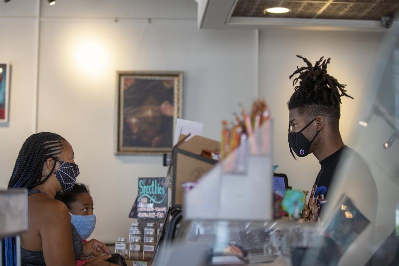 Urban Grind coffee shop employee Byron Reid, right, wears a mask as he serves Jerolyn Kight and her daughter Drew Kight in Atlanta,’s West Midtown community Thursday. (Alyssa Pointer/The Atlanta Journal-Constitution)
