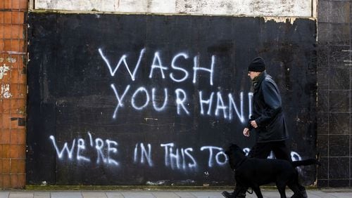 A man walks a dog past graffiti with the writing, “Wash Your Hands, We’re In This Together,” on the Lower Newtownards Road in Belfast, Northern Ireland, Tuesday March 24, 2020. LIAM MCBURNEY / PA VIA AP