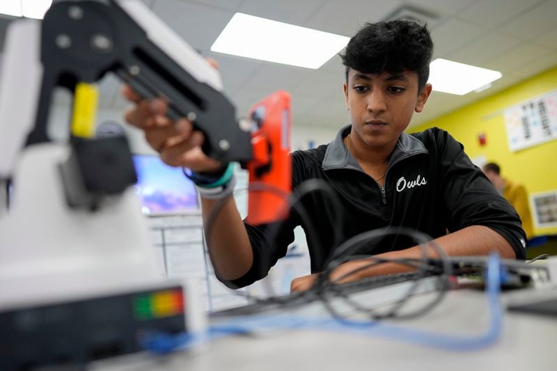 Eighth grader Anik Sahai, 14, tests and modifies code controlling a robotic arm, as he polishes the function of an app he created that uses a cellphone's camera to diagnose diabetic retinopathy, an eye disease that is a leading cause of blindness worldwide, in the Science Fair class at A.D. Henderson School in Boca Raton, Fla., Tuesday, April 16, 2024. Sahai's app took first place in the state's middle school science fair and is being considered for commercial use. (AP Photo/Rebecca Blackwell)