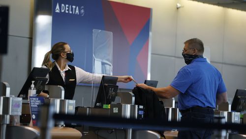 FILE - In this July 22, 2020 photo, a ticketing agent for Delta Airlines hands a boarding pass to a passenger as he checks in for a flight in the main terminal of Denver International Airport in Denver. .Air travel has collapsed because of the virus pandemic, and airlines are trying to convince passengers and their own employees about safety. All airlines require passengers to wear masks during flights, and most extend the rule to airports too. But some people have complained about violators refusing to keep their mask on .(AP Photo/David Zalubowski)