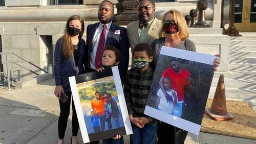 Family members of the late Antonio May and their lawyers stand on the steps of the Fulton County Courthouse in Atlanta on Nov. 16, 2021 following the indictment of six deputy sheriffs. In the foreground are two of May's three sons holding family photos. Top row from left, Shonna Rickerson, the boys' mother; attorneys Michael Harper and Teddy Reese; and April Myrick, legal guardian of both boys.
