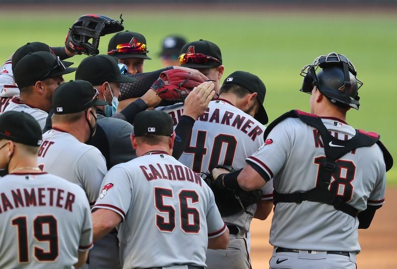 Arizona Diamondbacks starting pitcher Madison Bumgarner is swarmed by teammates as completed second game of a doubleheader without allowing a hit against the Braves Sunday, April 25, 2021, at Truist Park in Atlanta. Bumgarner's no-hit bid is not considered official by MLB because it was seven innings. (Curtis Compton / Curtis.Compton@ajc.com)