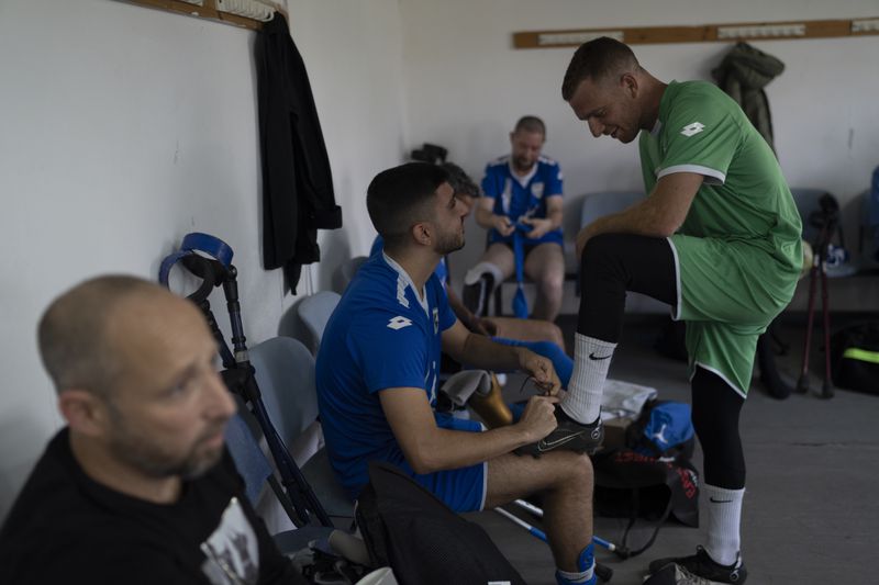 Or Hershkovits, goalkeeper of Israel Amputee Football Team, right, is helped by a teammate to tie his soccer cleat before a practice session in Ramat Gan, Thursday, April 11, 2024. Amputee football stands out as a disability sport because the athletes aren't in wheelchairs. It is played with six outfield players who have lower extremity amputations and play with crutches and without prosthetics. Each team also has one goalkeeper, who has an upper extremity amputation. The pitch is roughly half the size of standard.(AP Photo/Leo Correa)