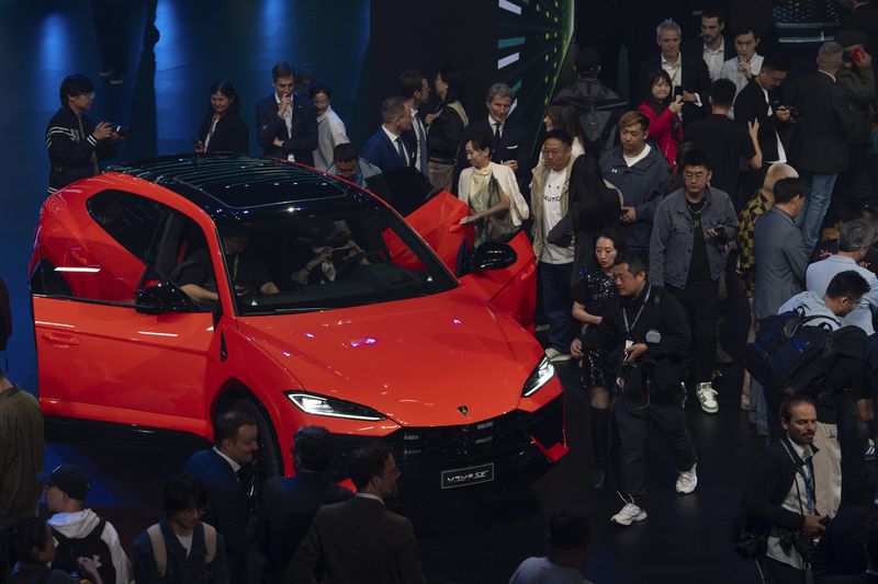 Attendees look at the Urus SE, the first hybrid plug-in version of the Lamborghini Super SUV, shown at a Volkswagen Group media event held a day before the auto show in Beijing, Wednesday, April 24, 2024. The Volkswagen Group, which includes Audi and Porsche, plans to launch 40 new models in China over the next three years and to have a lineup of 30 EVs by 2030. (AP Photo/Ng Han Guan)