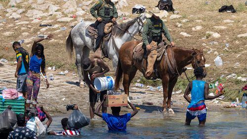 U.S. Border Patrol agents interact with Haitian migrants on the bank of the Rio Grande in Del Rio, Texas, on Monday. As U.S. immigration authorities began deporting migrants back to Haiti from Del Rio, thousands more waited in a camp under an international bridge in Del Rio, while others crossed the river back into Mexico to avoid deportation. (John Moore/TNS)