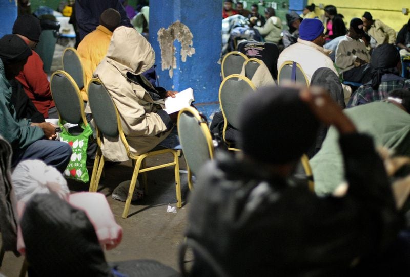 A man reads a book, surrounded by hundreds of other people spending the day in the overflow room at the homeless shelter on Pine Street near the intersection with Peachtree Street in Atlanta. (Jason Getz / AJC file photo / December 2011)